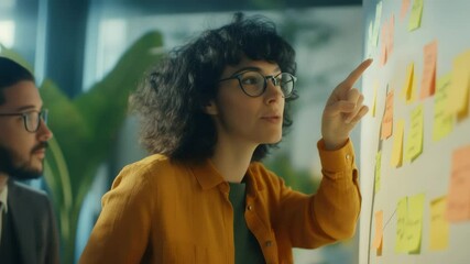 Confident project manager pointing at colorful sticky notes, explaining strategic plan to attentive colleague in contemporary workspace, highlighting teamwork dynamics