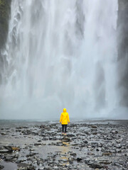 Vibrant yellow raincoat contrasts against Skogafoss waterfall in Iceland