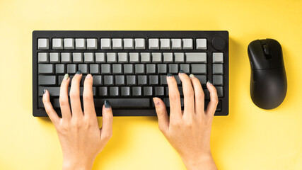 Hands typing on a black mechanical keyboard with gray keycaps, accompanied by a wireless mouse on a...