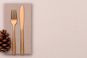 Elegant golden cutlery set on a stylish linen napkin with a pinecone