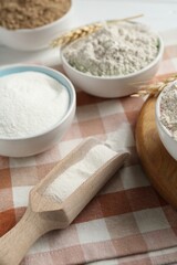 Different types of flour in bowls and scoop on table, closeup