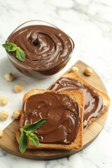 Tasty chocolate spread with mint and hazelnuts on white marble table, closeup