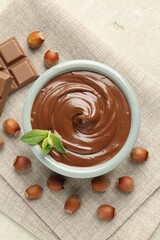 Tasty chocolate spread, pieces, mint and hazelnuts on light table, flat lay