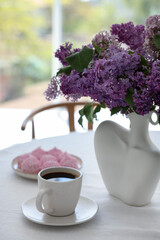 Bouquet of beautiful lilac flowers, coffee and dessert on white table indoors