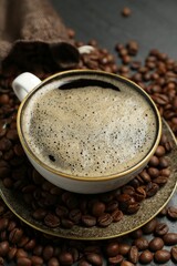 Aromatic coffee in cup and beans on table, closeup