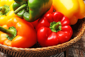 Fresh colorful bell peppers in wicker basket on table, closeup
