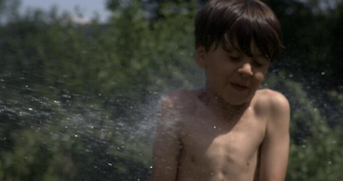 Shirtless young boy flinching with eyes closed as water spray hits chest outdoors, captured in super slow motion with high-speed camera
