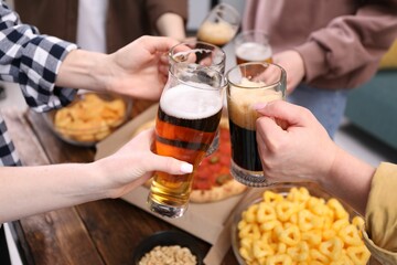 Friends clinking glasses of beer at wooden table, closeup