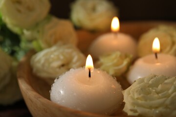 Burning candles, water and rose flowers in wooden bowl on table, closeup