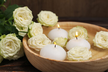 Burning candles, water and rose flowers in bowl on wooden table, closeup