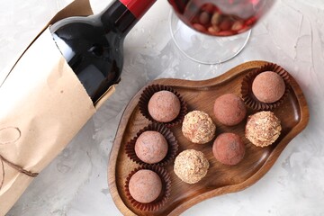 Delicious truffle bonbons and red wine on light grey background, flat lay