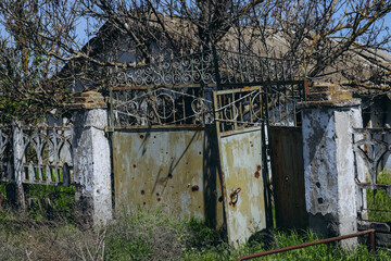 Destroyed, war-torn, abandoned — a completely ruined house and shrapnel-riddled gates stand...
