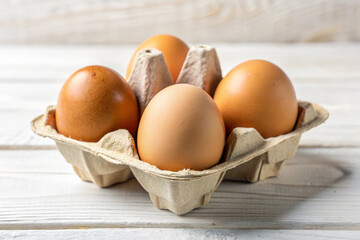 Four fresh brown eggs in a cardboard carton sit on a white wooden surface