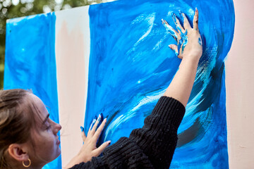 Young female with fair hair, engaging in expressive painting using hands. Dynamic blue strokes...