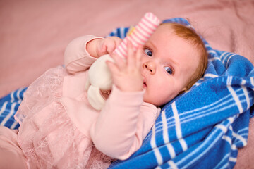 Young female child with light hair and fair skin lying on blue blanket. Holding plush toy while looking up with curious eyes. Soft lighting enhances gentle expression