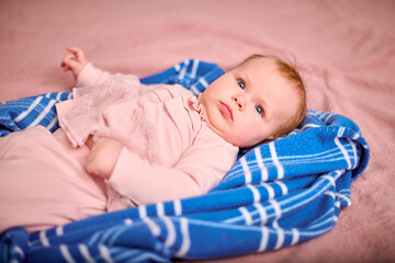 Infant female with red hair and fair skin lies on blue striped blanket. Soft lighting highlights pink outfit, creating serene and cozy setting