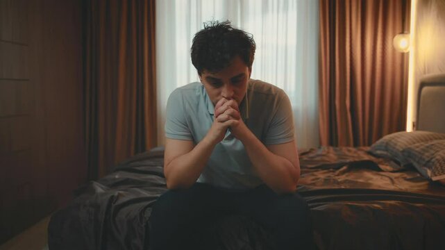 portrait upset face unhappy man sitting on bed in dark room bedroom, mood depression sadness emotion. Sad lonely guy feels bad after party, migraine suffers headache insomnia. mental health bad sleep