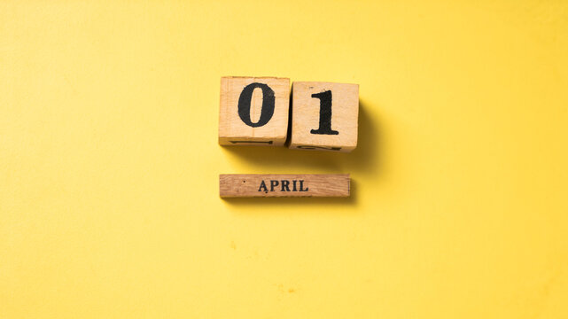 Wooden blocks showing the date April 1 on a vibrant yellow background. A symbolic flat lay representing April Fool’s Day with a playful and minimalist aesthetic