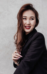A young woman with long hair and braces smiles confidently in a black blazer