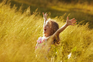 Happy little girl in tall grass in a field on a summer evening.
