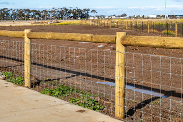 A wooden post and wire mesh fence lines the edge of a cleared, undeveloped suburban block in outer...
