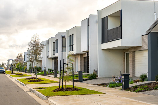 A quiet residential street lined with modern double-storey townhouses in a newly developed outer suburb. Contemporary urban planning and real estate investment in Australia’s growing suburban fringe. - Powered by Adobe