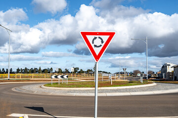 A roundabout with a yield sign stands at the center of a newly developed suburban road of an outer suburban estate in Australia.  Clear traffic signage and road design reflect planned urban expansion  © Doublelee