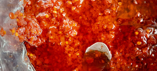 Spicy red sambal with chili seeds and oil, captured in a close-up shot. A bold and flavorful Indonesian chili condiment