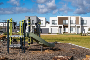 Modern double-storey townhouses near a children’s playground and a landscaped suburban park. A...
