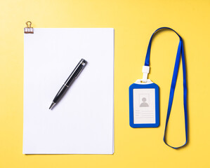 Top view of a blue ID card with lanyard, a black pen on top of clipped white papers, all neatly...
