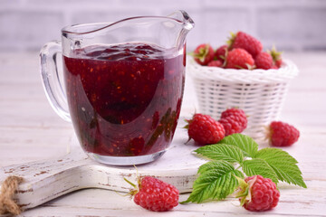 Raspberry jam in a glass sauceboat on a white wooden background.
