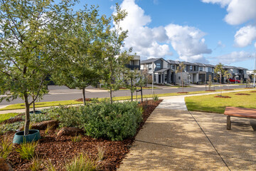 A landscaped public space with walking path, young trees, and modern two-storey townhouses in a new residential development in suburban Australia. Green infrastructure in a growing neighborhood.