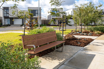 A public bench in a landscaped green space in a newly developed suburban estate with a row of...