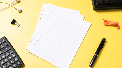 Flat lay of office desk items including lined paper, pen, keyboard, calculator, earbuds, and a...