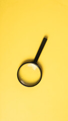 A black magnifying glass placed diagonally on a bright yellow background, commonly used for...