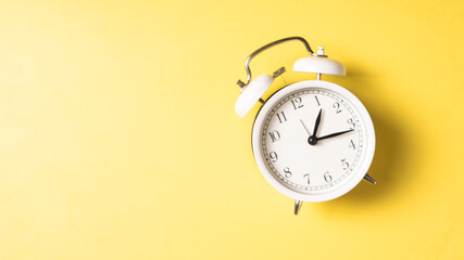A classic white twin-bell alarm clock showing 10:00, placed neatly on a bright yellow background...