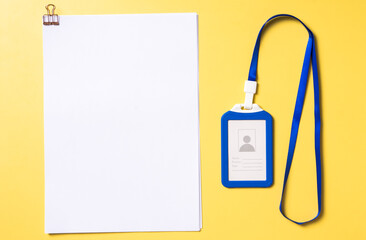 Flat lay of a blue ID card holder with lanyard and stacked blank white papers clipped together,...