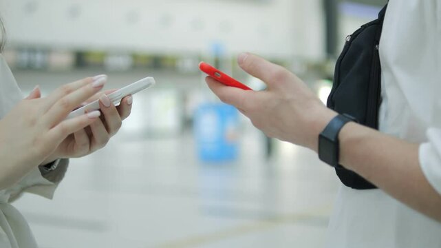 Two people are talking on their cell phones in a public place. One of the phones is red