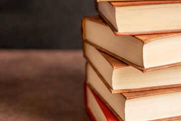 Pile of stacked hardcover books on dark brown table against black wall with copy space at reading...