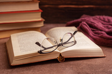 Reading glasses resting on an open book with a stack of books and a sweater in the background on...
