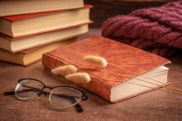 A still life with pile or stack of books, closed book, eyeglasses, autumn sweater and dried flowers...