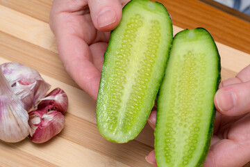 Freshly cut cucumber halves and garlic on a wooden cutting board