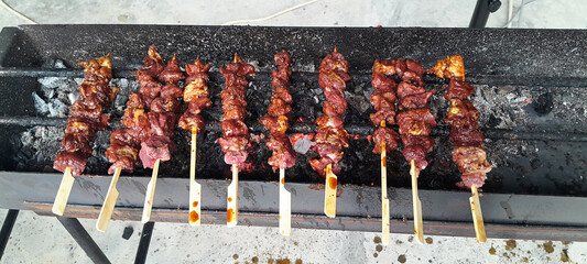 A row of juicy meat skewers (satay) being grilled over hot charcoal on a traditional open grill. The meat is glazed and caramelized, showcasing a popular Southeast Asian street food.