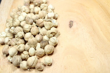 A close-up pile of dried white cardamom pods on a light wooden background, emphasizing their...