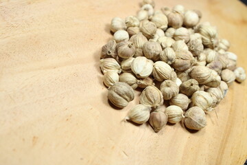A close-up pile of dried white cardamom pods on a light wooden background, emphasizing their...