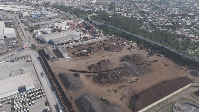 Aerial footage showcasing scrap piles, heavy machinery, freight containers, and surrounding industrial infrastructure in a shipyard.