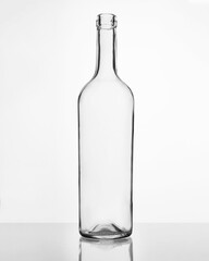 Elegant clear glass wine bottle with narrow neck on reflective white surface, studio-lit minimal commercial shot for premium beverage branding