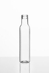 Clear square-shaped glass bottle for olive oil or balsamic vinegar... on reflective white surface, studio-lit commercial mockup