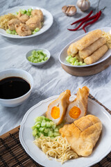 Asian-style assorted pempek dishes including kapal selam, lenjer, and adaan served with noodles, diced cucumber, and vinegar sauce, styled on a marble background with garlic and chili