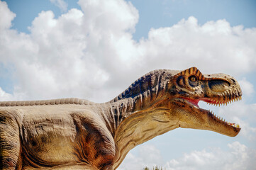 A huge tyrannosaurus dinosaur, a close-up of the dinosaur's head against the sky and clouds